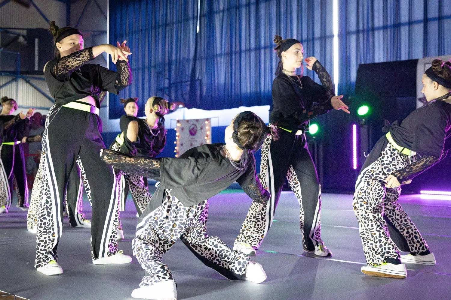 Grupa nastoletnich tancerek w dynamicznym układzie choreograficznym na scenie.
