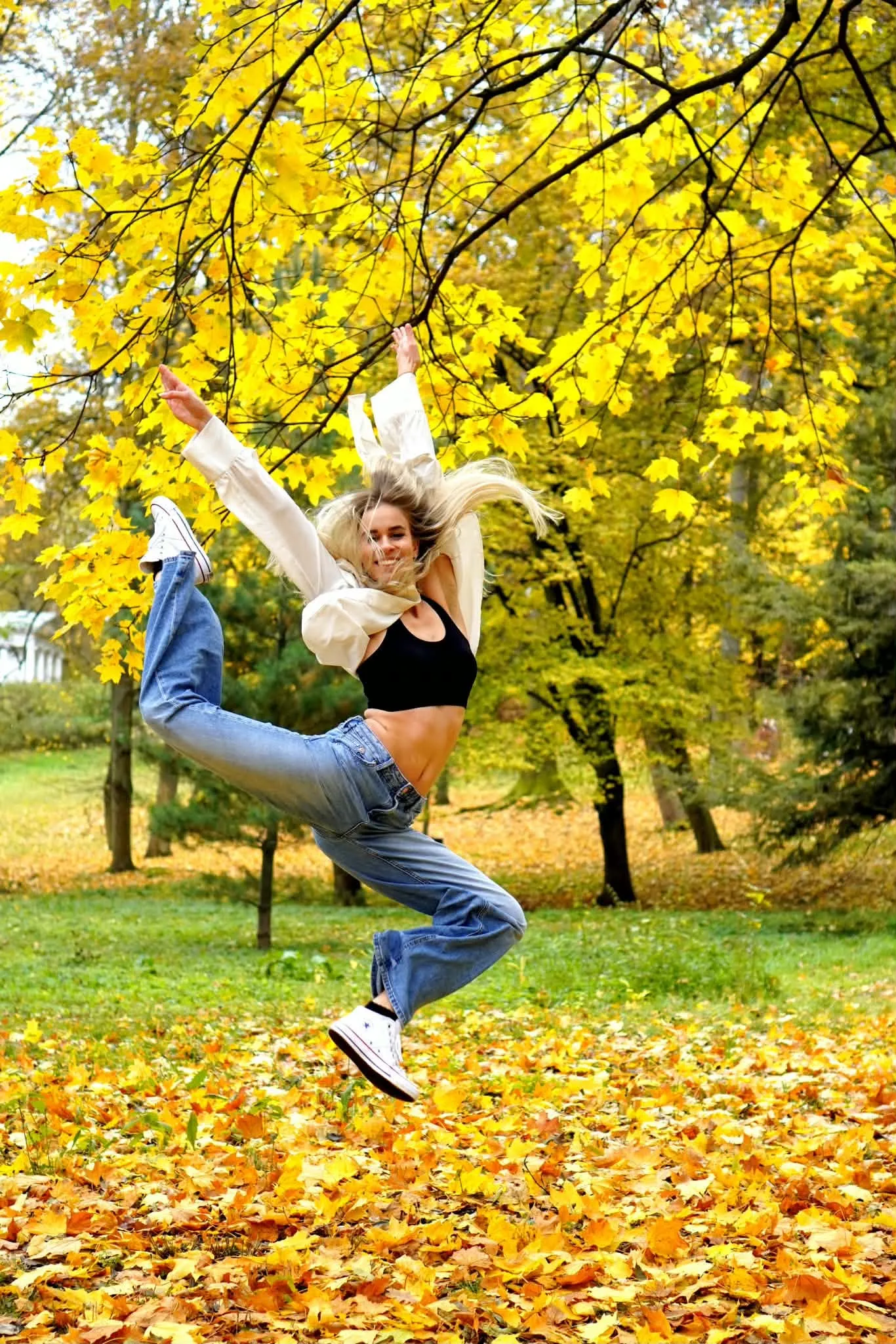 Tancerka w energicznym skoku, z rękami w górze i nogą uniesioną w kopnięciu, jesienny plener z żółtymi liśćmi — Raion Dance Academy